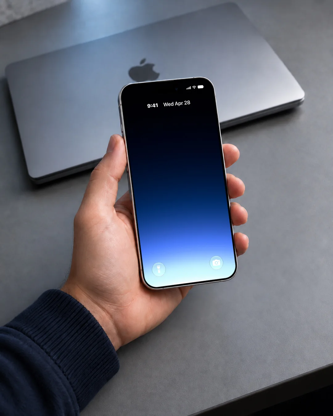 A Gradient wallpaper on a phone held in one hand over a closed laptop, blue rising from the bottom edge